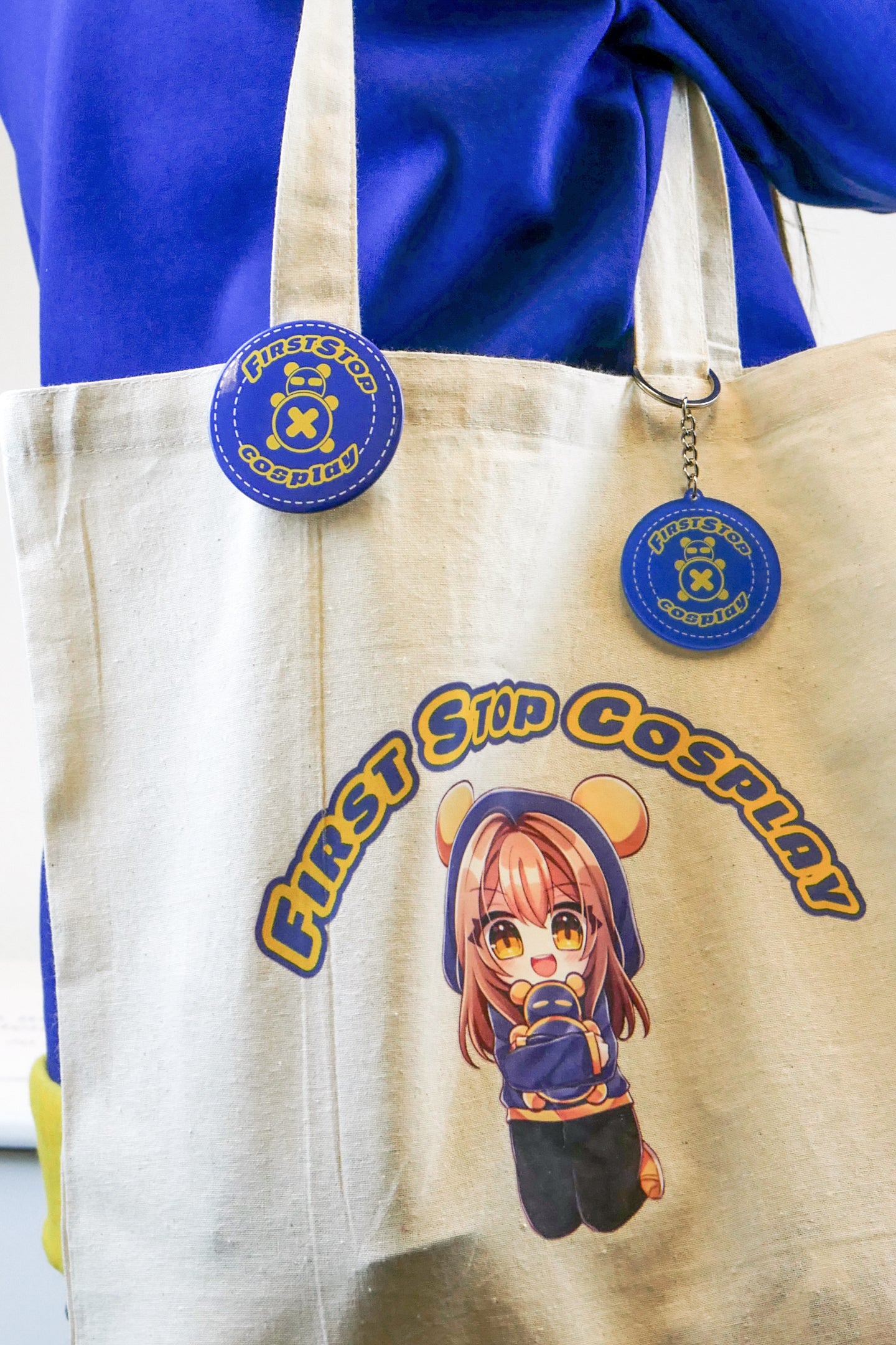 A lifestyle image of the Pan and Dah Tote Bag. Pan's side is showing, with a Circle Stitch Logo button hanging from one side of the tote strap and a Circle Stitch Logo keychain hanging from the other side of the strap. The bag is slung over a person's shoulder.