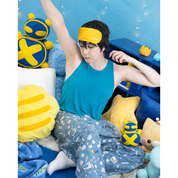Photo of male model, matthew_aizel, wearing a sewing-themed pair of Pajama Pants and a teal crop top. He is stretching among a corner of cushions. The image elicits a feeling of sleepiness.