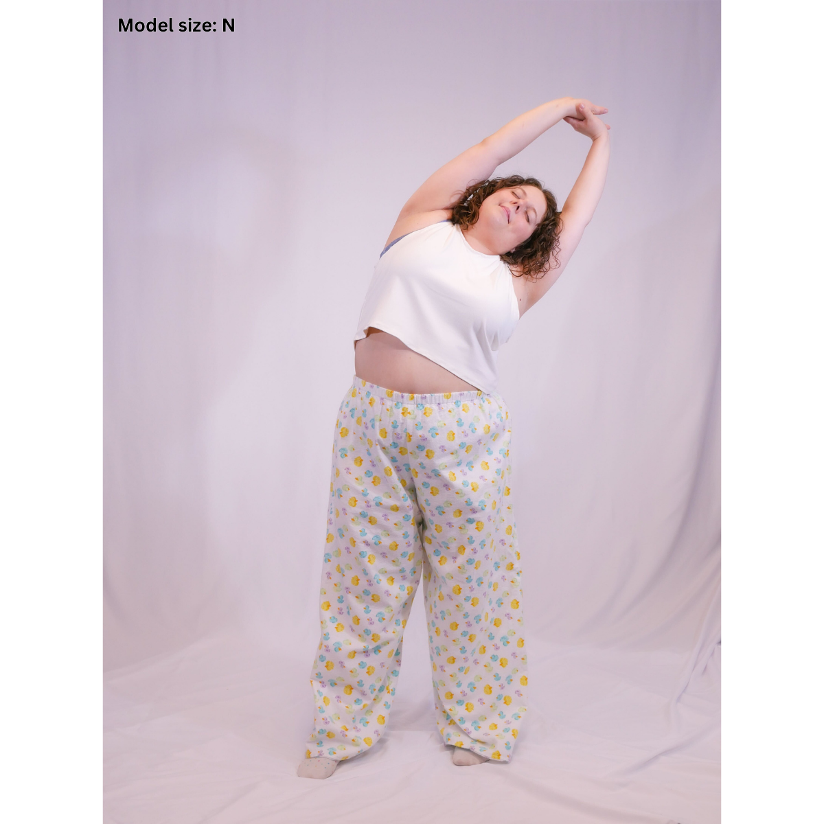 A photo of a woman wearing rubber ducky white pajama pants (size N) and a white sleeveless crop top (size H).