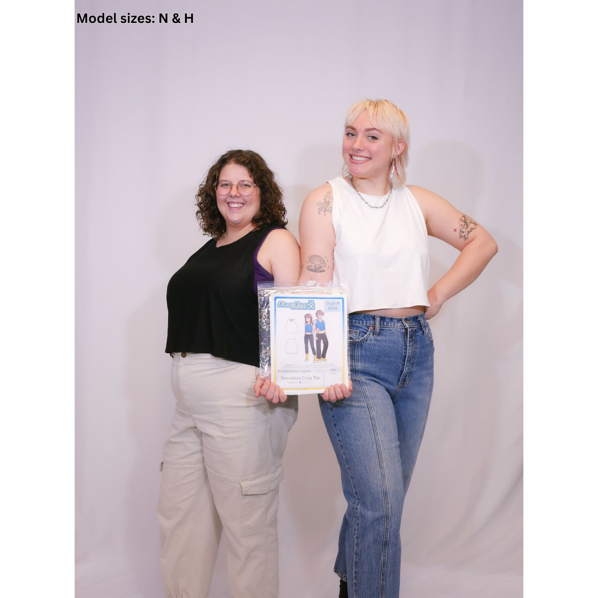 A photo of 2 people holding the packaging. One wearing a black sleeveless crop top (Size N) with beige pants, and the other wearing a sleeveless crop top (size H) with jeans.