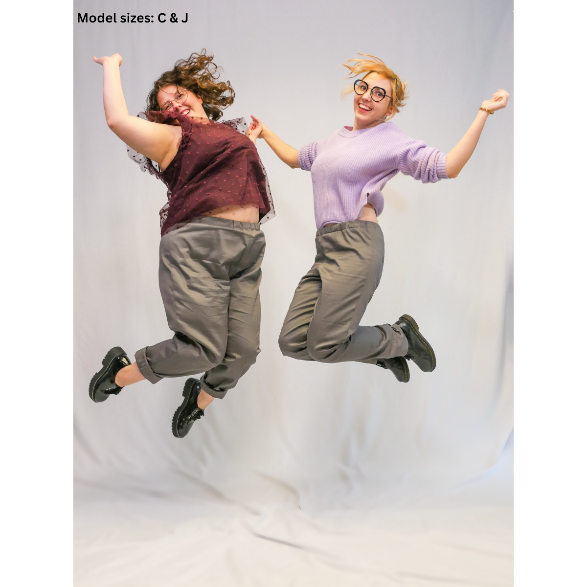 A female size J model and nonbinary size C model jumping in the air while wearing completed Pants. Their arms are out and they're both smiling.