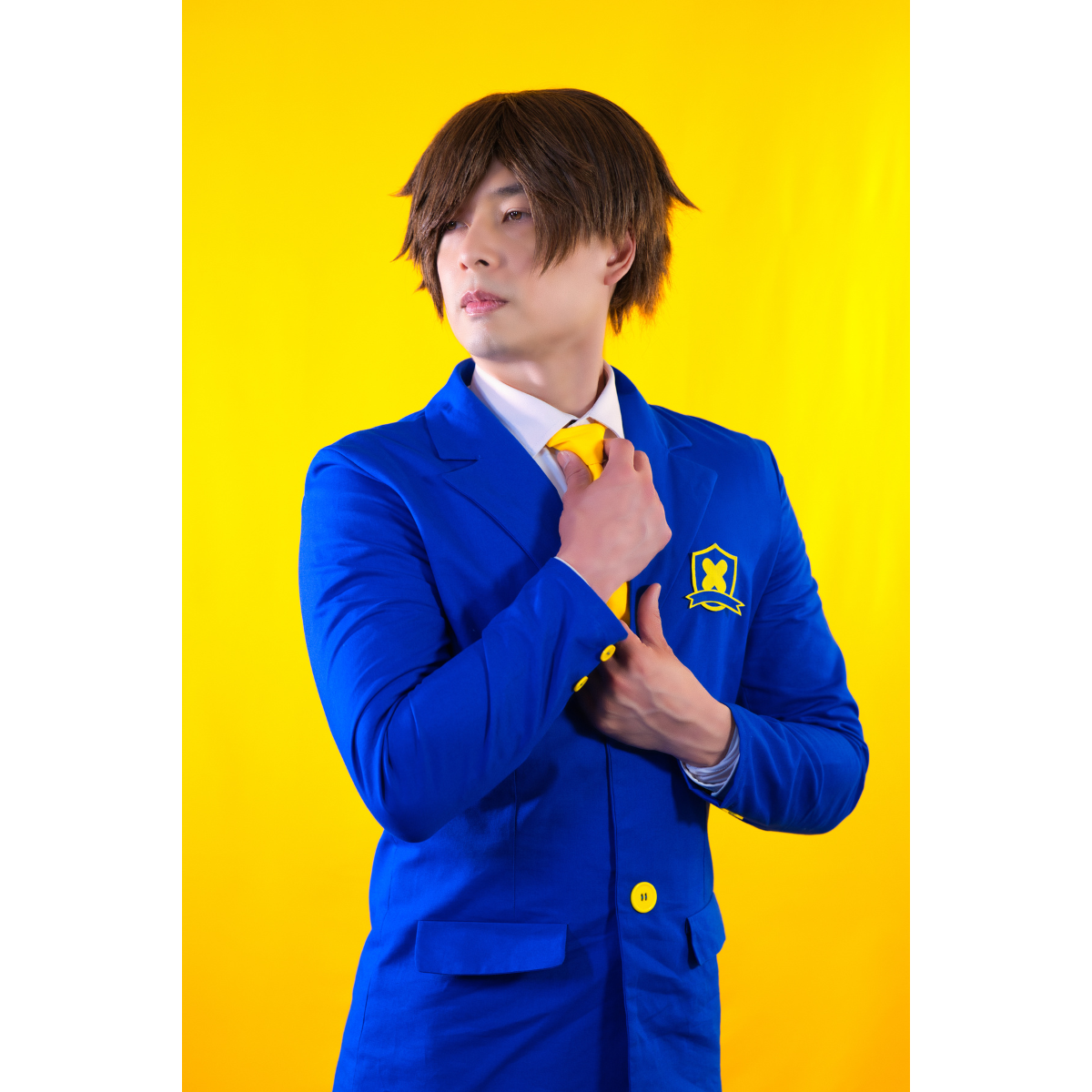 Male model (size E) posing in the Blazer. He is adjusting a necktie, displaying the buttons on the sleeve cuffs, pockets, and front closure buttons.
