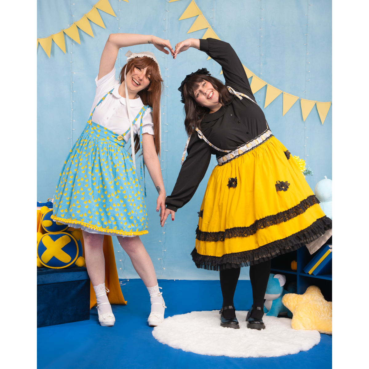 Two models (size C and size J) posing in different versions of the Lolita Blouse and skirt. They're leaning toward each other and using their arms to make a large heart. The model on the left's blouse is short-sleeved, while the model on the right has long sleeves.