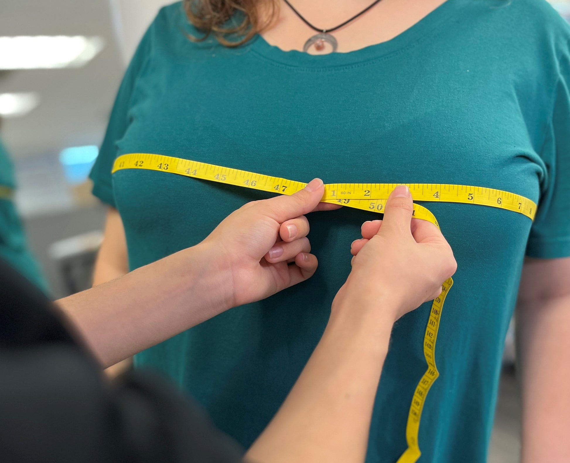 Tape measure being displayed by seamstress measuring a woman's bust.