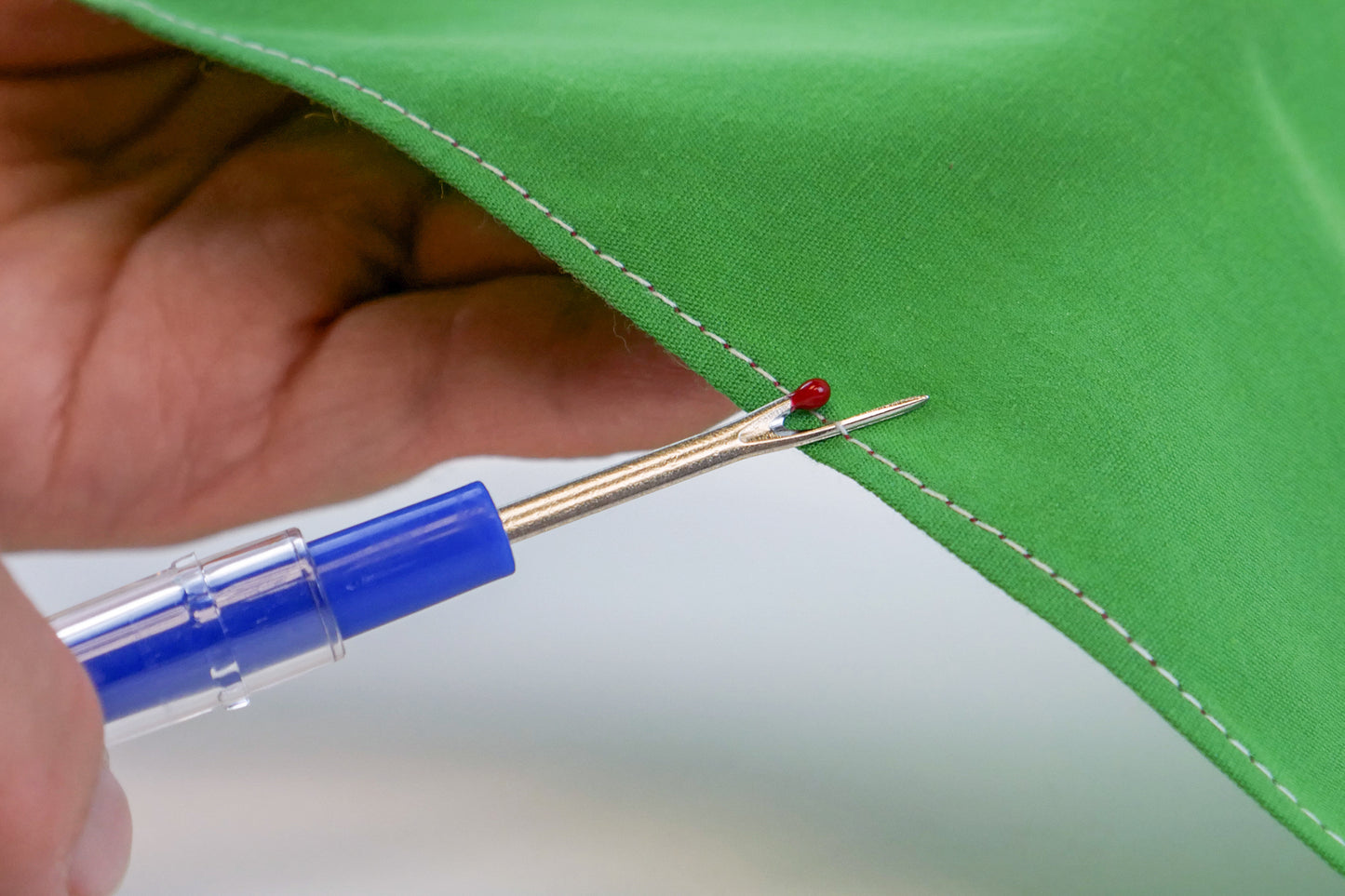 A lifestyle image of hands holding the seam ripper to rip a white thread seam on green fabric.