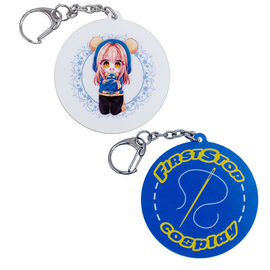 The front and back of the Pan keychain. Pan is a female character in chibi form, crouching on her knees, and holding a small Timmy figure. She is smiling. The back of the keychain says "First Stop Cosplay" with a sewing needle in the middle.