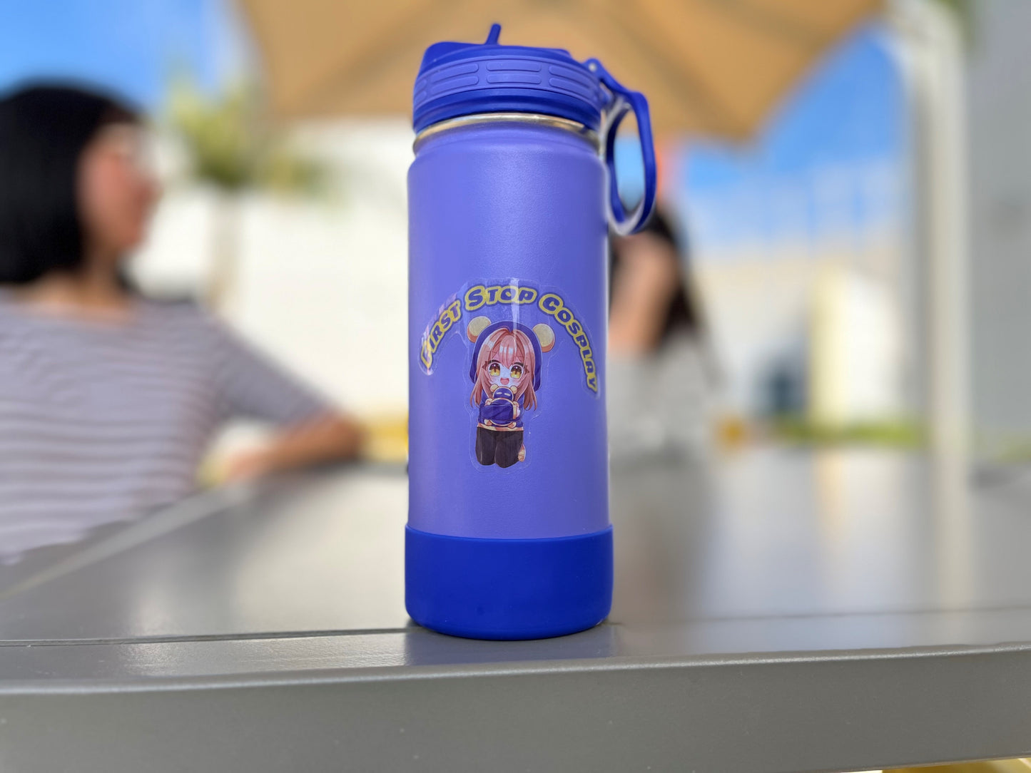 A "Pan" sticker on a purple water thermos with two people chatting in the background.